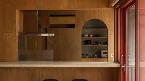 Eine moderne Küche mit Holzschränken, einer Edelstahl-Dunstabzugshaube und einem eingebauten Backofen. Zwei schwarze Hocker stehen an der Arbeitsplatte.