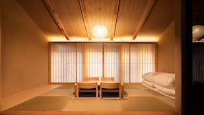 Et traditionelt japansk rum med tatamimåtter, et lavt træbord med stole, en futon-madras og shoji-skærme.