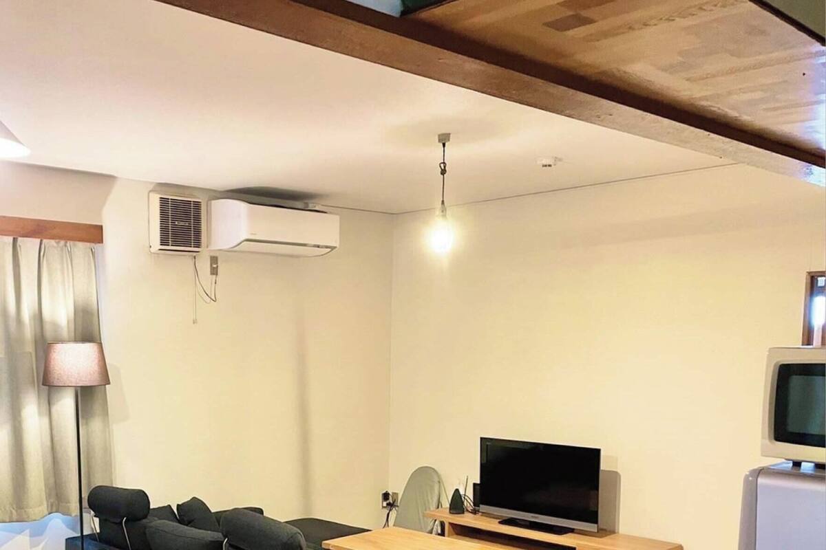 Una habitación de hotel con cama, escritorio con computadora, televisor, aire acondicionado y ventana con cortinas.