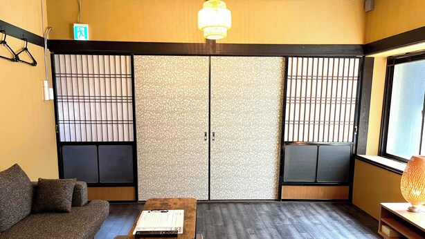 A traditional Japanese room with tatami flooring, a low table, a sofa, sliding doors, and a hanging light fixture. - Garando (Hakodate)