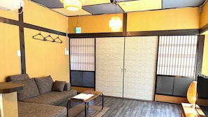 A room with a sofa, a small table, a TV, and sliding doors with a patterned view. - Garando (Hakodate)