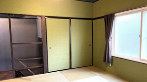 A room with tatami flooring, a sliding door, a window with curtains, and a ladder against the wall. - Garando (Hakodate)
