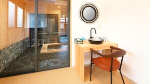 A bathroom with a wooden vanity, a round mirror, and a stone-tiled shower area.