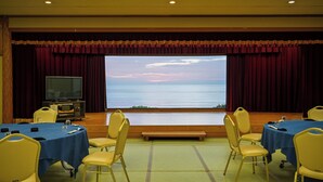 Un salón de conferencias con una pantalla grande mostrando un paisaje, sillas amarillas y mesas con manteles azules.