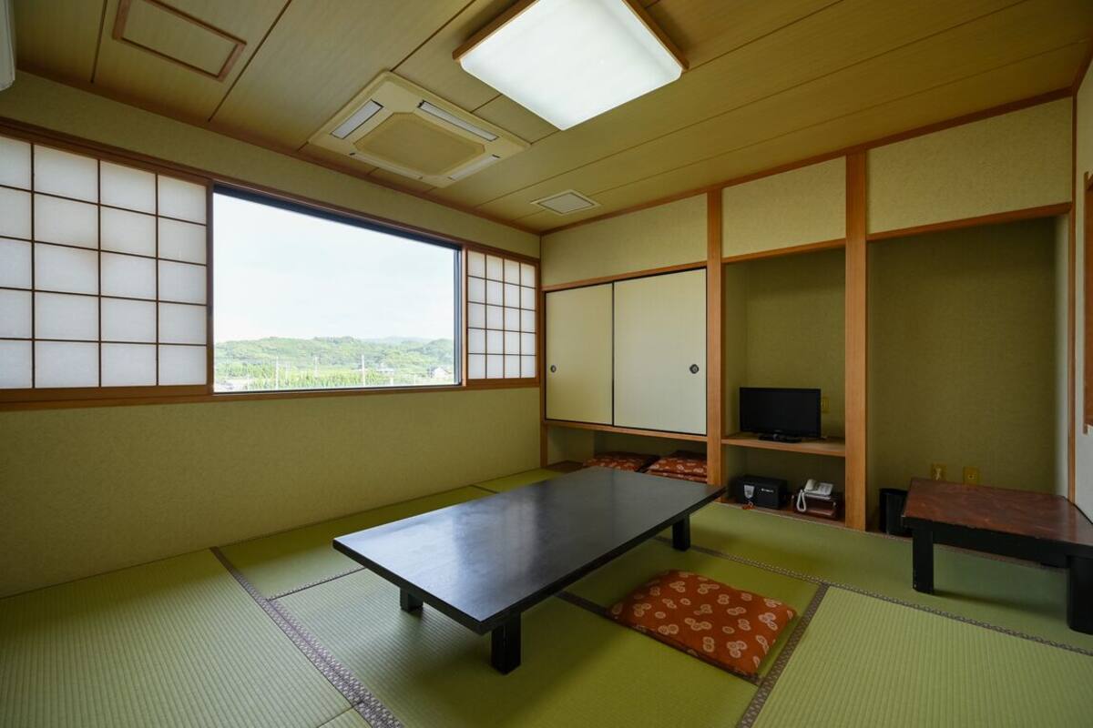 Una habitación con esteras de tatami, una mesa baja, un televisor y vistas a colinas verdes.