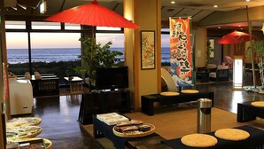 Vestíbulo de hotel con vista al océano, una recepción, áreas de descanso y un bufé con diferentes opciones de comida.
