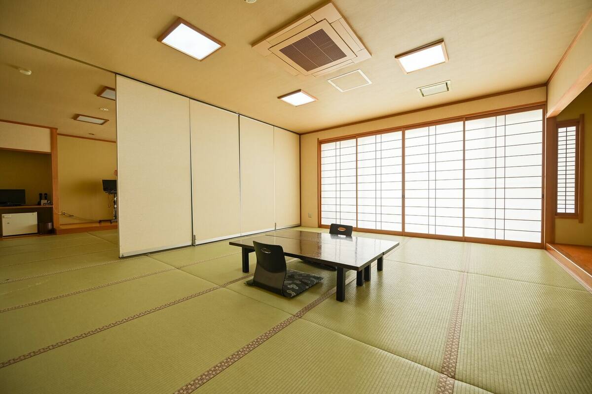 Una habitación con esteras de tatami, una mesa baja y sillas, puertas correderas y un ventanal grande.