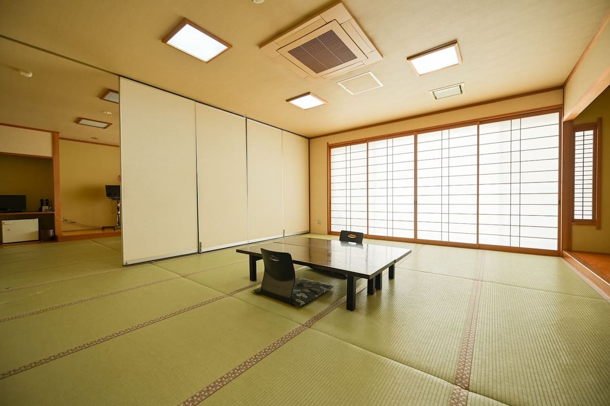 Una habitación con esteras de tatami, una mesa baja y sillas, puertas correderas y un ventanal grande.