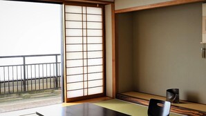 Una habitación con esteras de tatami, una mesa baja, dos sillas y un puertas correderas.