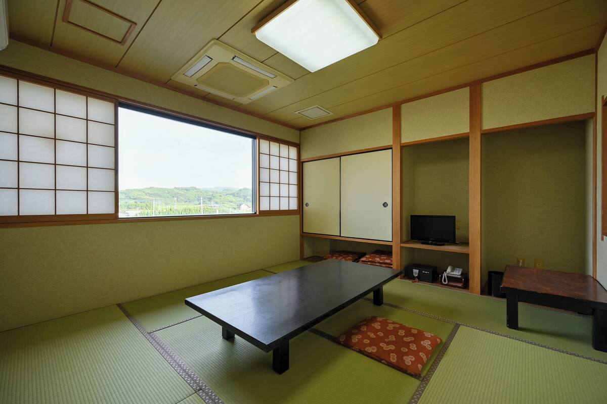 Una habitación japonesa tradicional con suelo de tatami, una mesa baja, un televisor y puertas correderas.