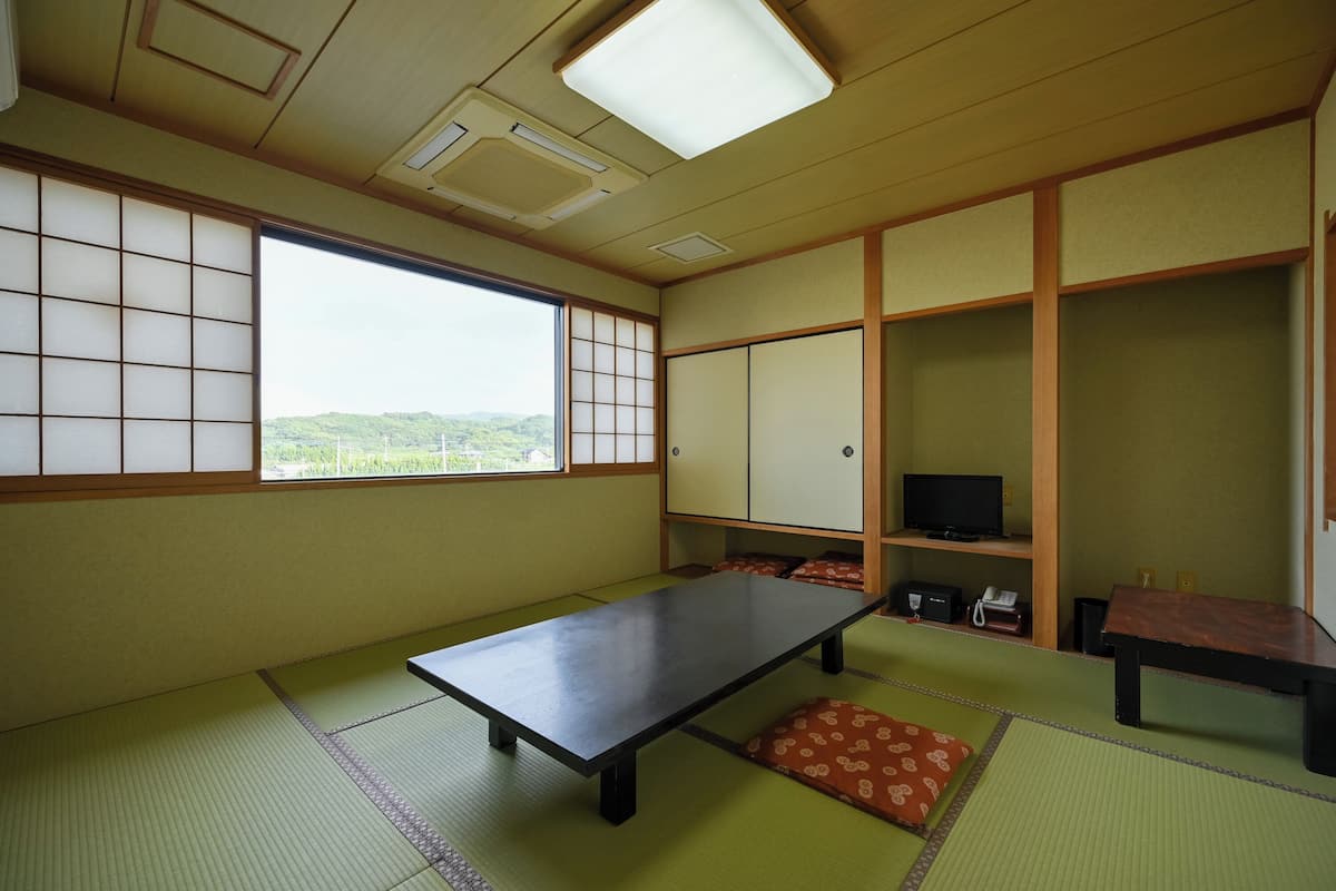 Una habitación japonesa tradicional con suelo de tatami, una mesa baja, un televisor y puertas correderas.