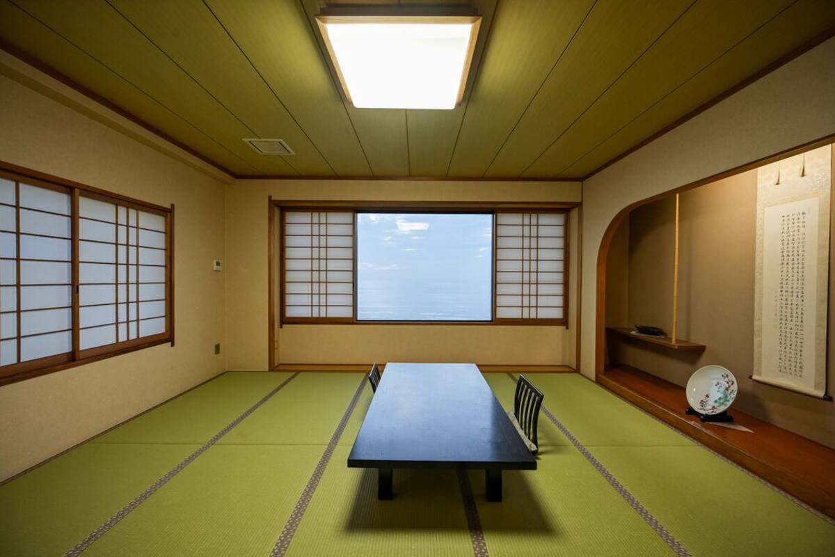 Una habitación con esteras de tatami, una mesa baja, paneles shoji y vista al cielo.