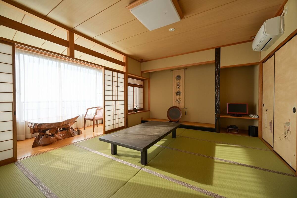 Una habitación con tatamis, una mesa baja, puertas correderas, un televisor y decoración japonesa tradicional.