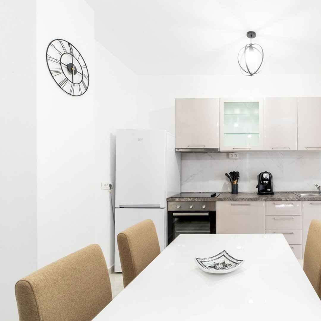 Une cuisine moderne avec des meubles blancs, un réfrigérateur blanc, une cuisinière et une machine à café posée sur le plan de travail.
