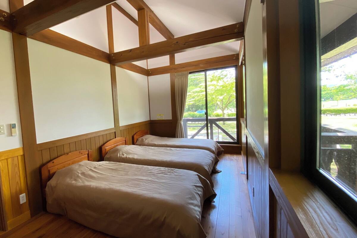 Ein Zimmer mit Holzbalken, zwei Betten, einem Fenster mit Blick ins Grüne und einer Tür.