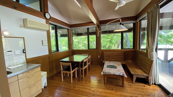 A wooden interior with a dining table, chairs, a bench, and large windows offering a view of greenery. - Tabino Teitaku Yakurai Cottage (Kami)
