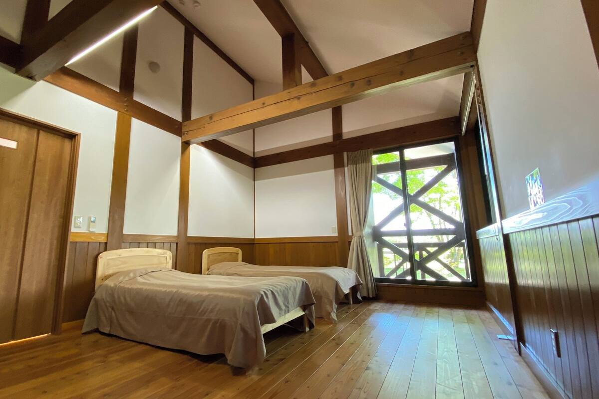 Ein Zimmer mit zwei Betten, Holzbalken, einem großen Fenster mit Aussicht und einer Tür.