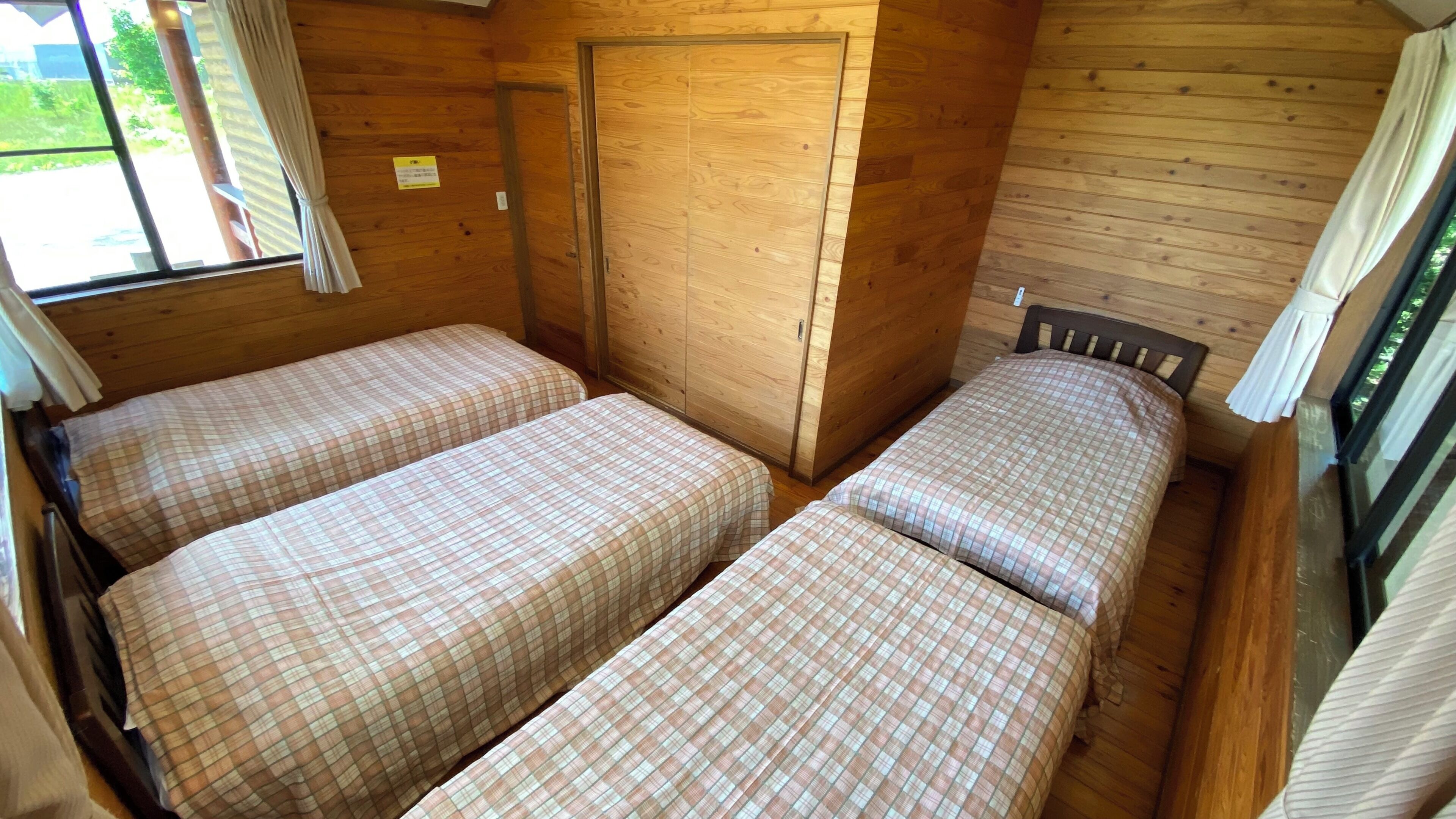 A cabin with two beds, wooden walls, a window, and a door.