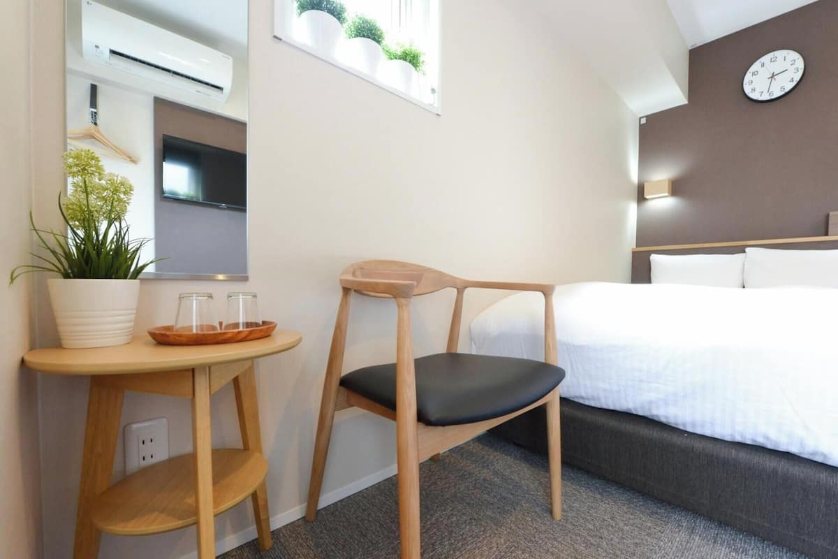 Een hotelkamer met een bed, een houten stoel, een klein tafeltje met een plant, een televisie en een wandklok.