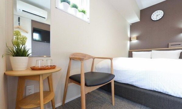 Een hotelkamer met een bed, een houten stoel, een klein tafeltje met een plant, een televisie en een wandklok.