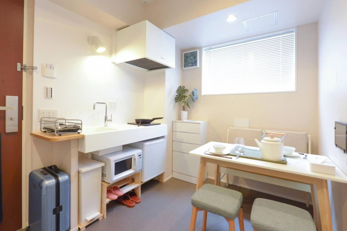 Een kleine keuken met een magnetron, spoelbak en een eethoekje met een tafel en stoelen.
