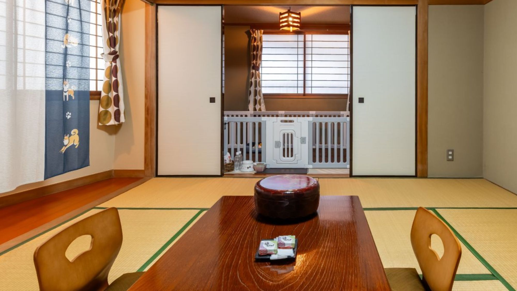 A traditional Japanese room with tatami flooring, a wooden table with a round tray, and a sliding door leading to a kitchen area.