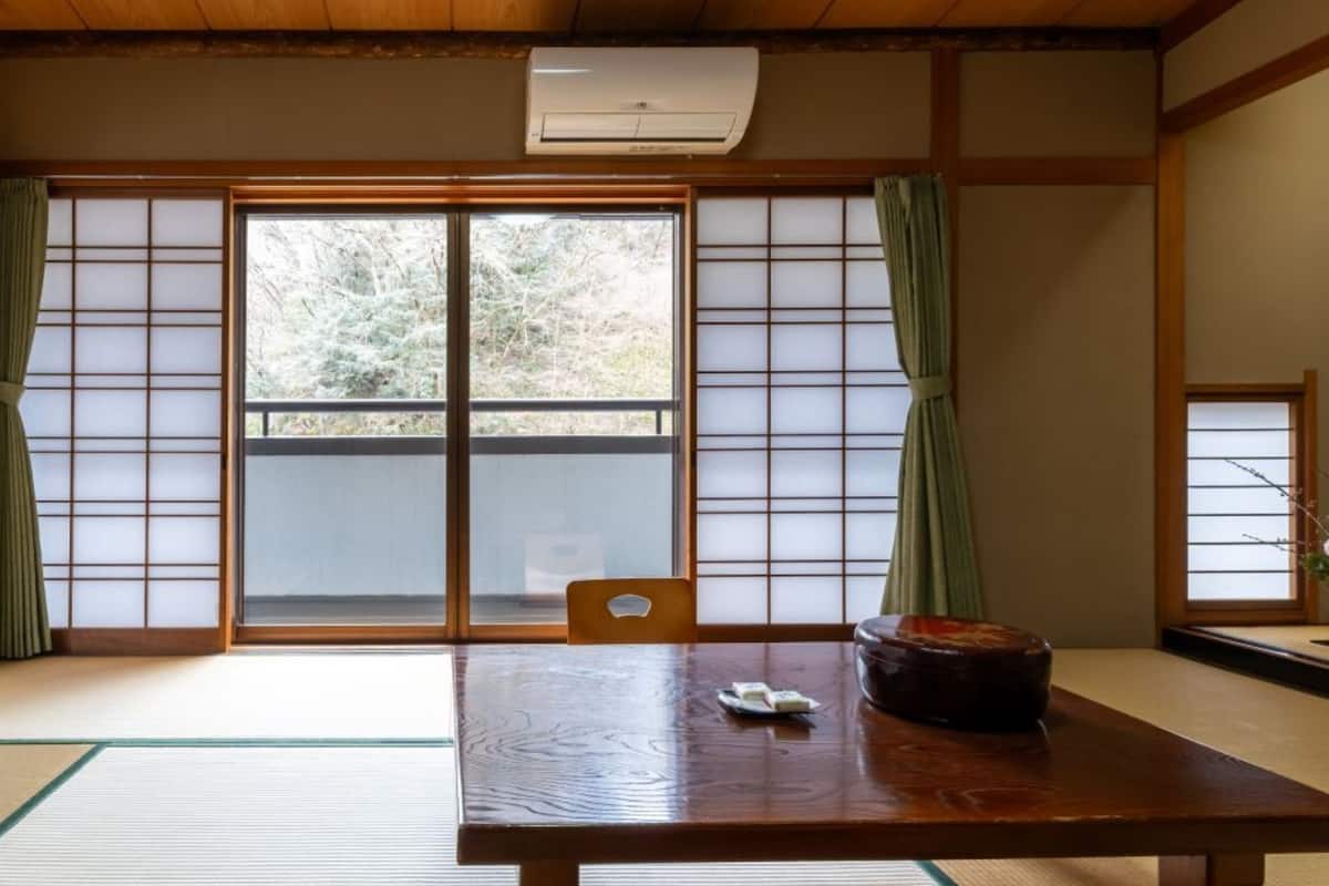 Ein traditioneller japanischer Raum mit Tatami-Böden, Schiebetüren, einem Holztisch und einer kleinen Tischlampe.