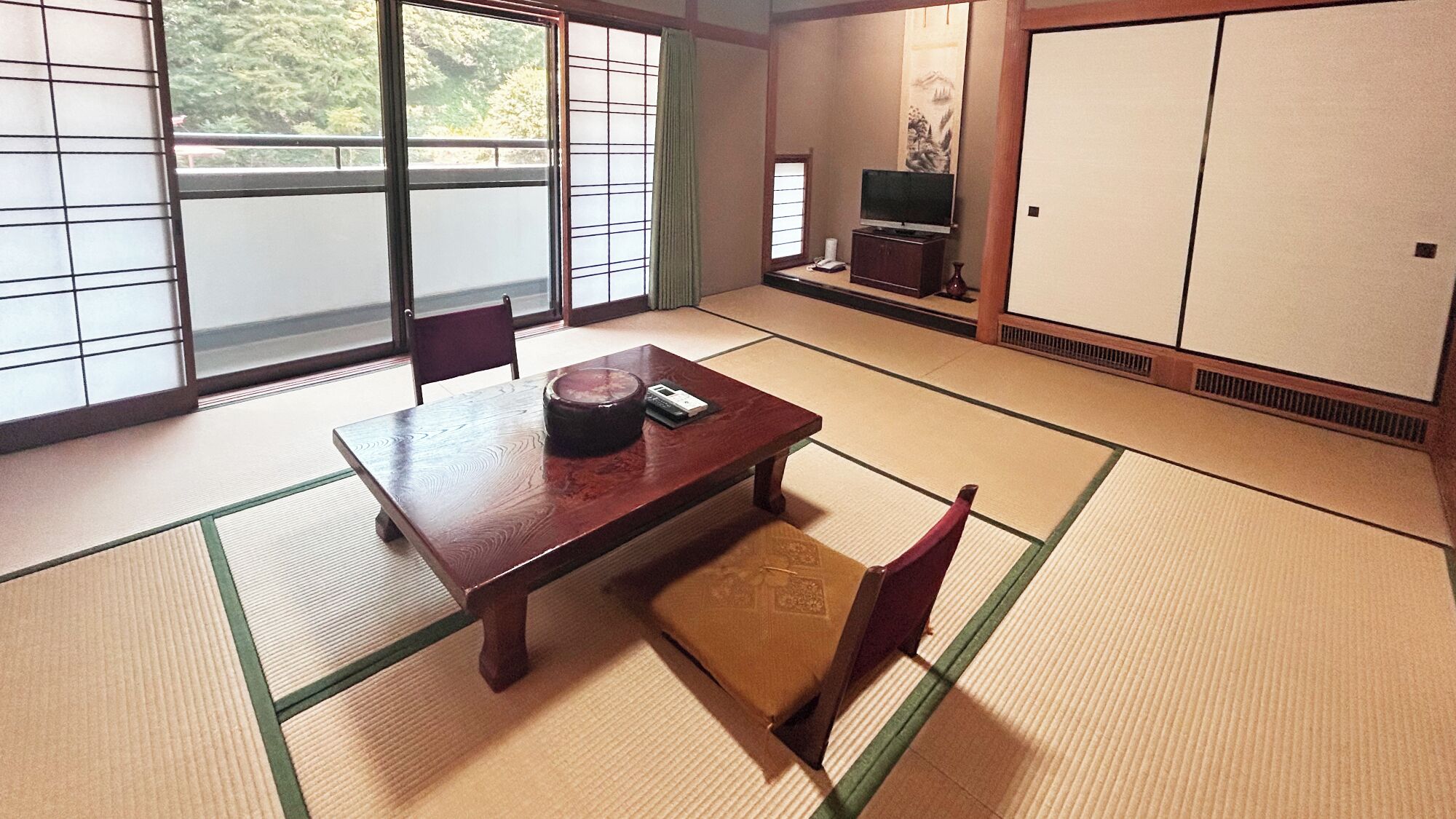 A traditional Japanese room with tatami flooring, a low wooden table, and a television on a stand.