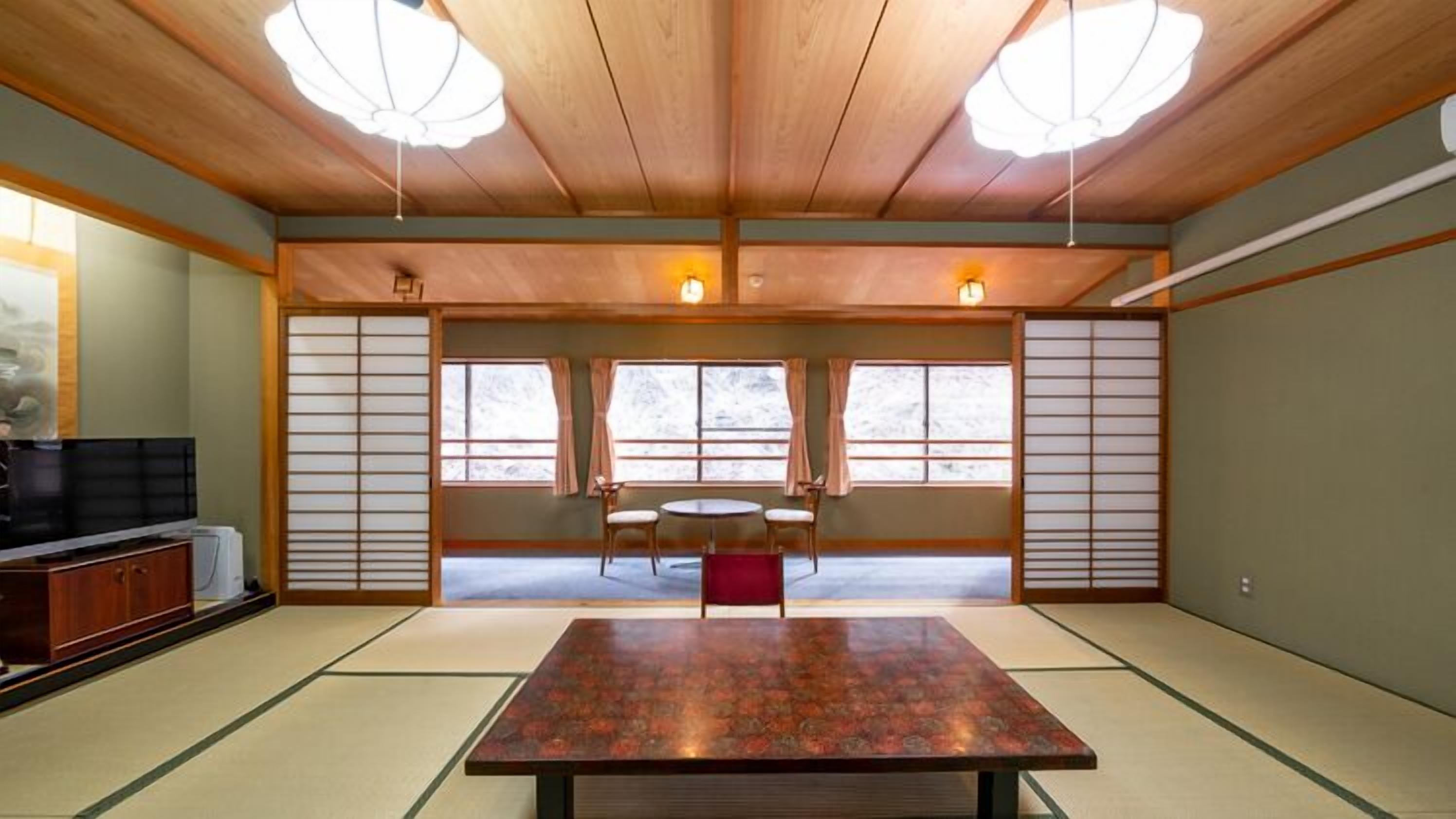 A traditional Japanese room with tatami flooring, a low table, two chairs, and sliding doors.