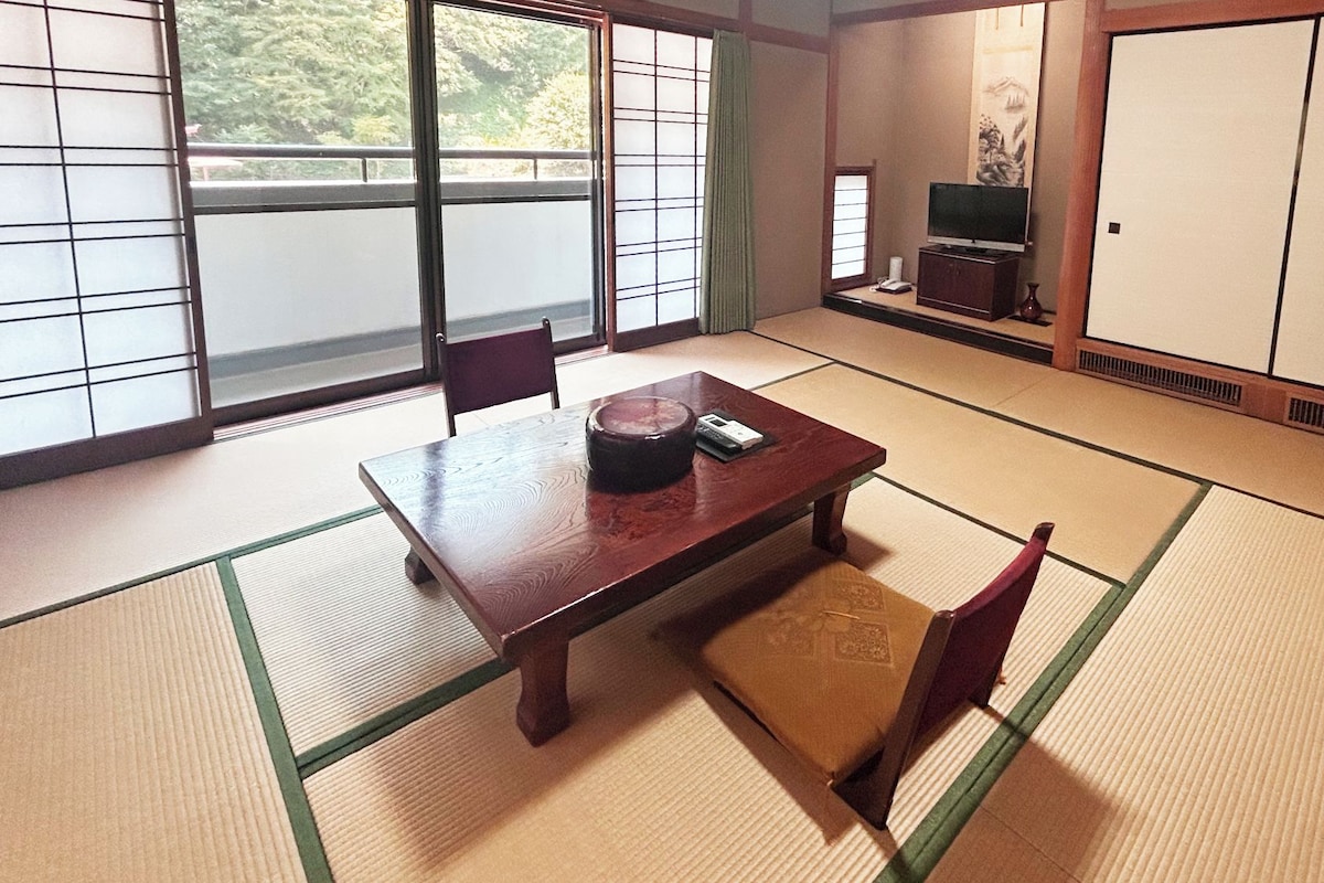 Una habitación tradicional japonesa con suelo de tatami, una mesa de madera baja y un televisor sobre un mueble.