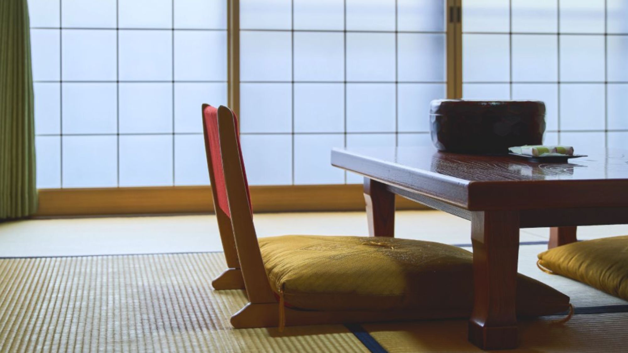 A traditional Japanese room with tatami flooring, a low table, and a wooden chair.