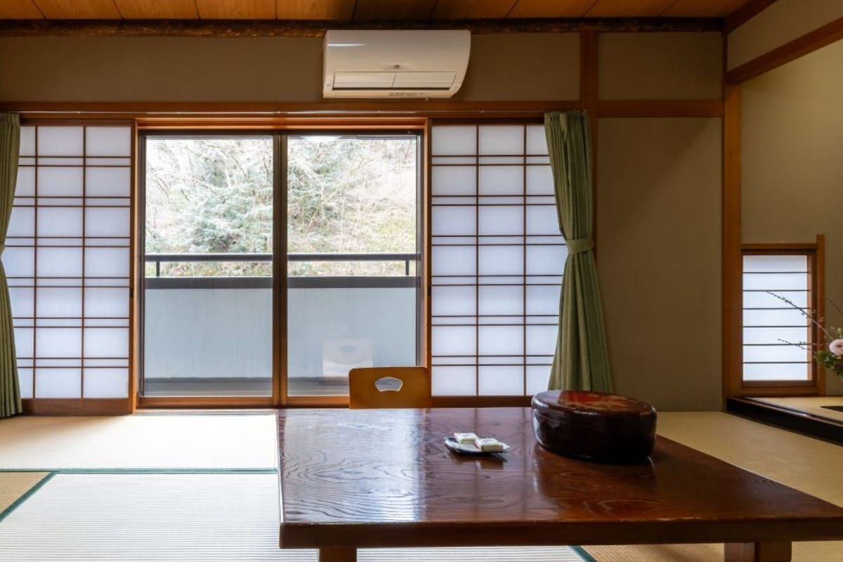 Una habitación japonesa tradicional con suelo de tatami, puertas correderas, una mesa de madera y una lámpara de mesa pequeña.