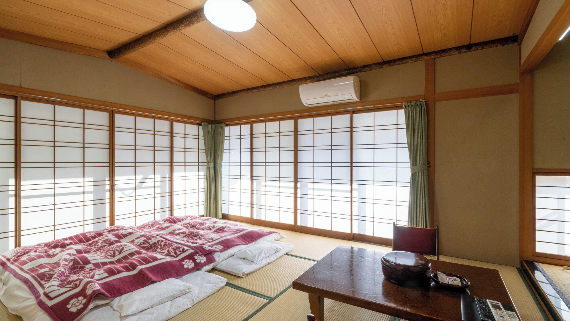 A traditional Japanese room with tatami flooring, a futon bed, a shoji screen, a wooden table with a kettle, and an air conditioning unit.