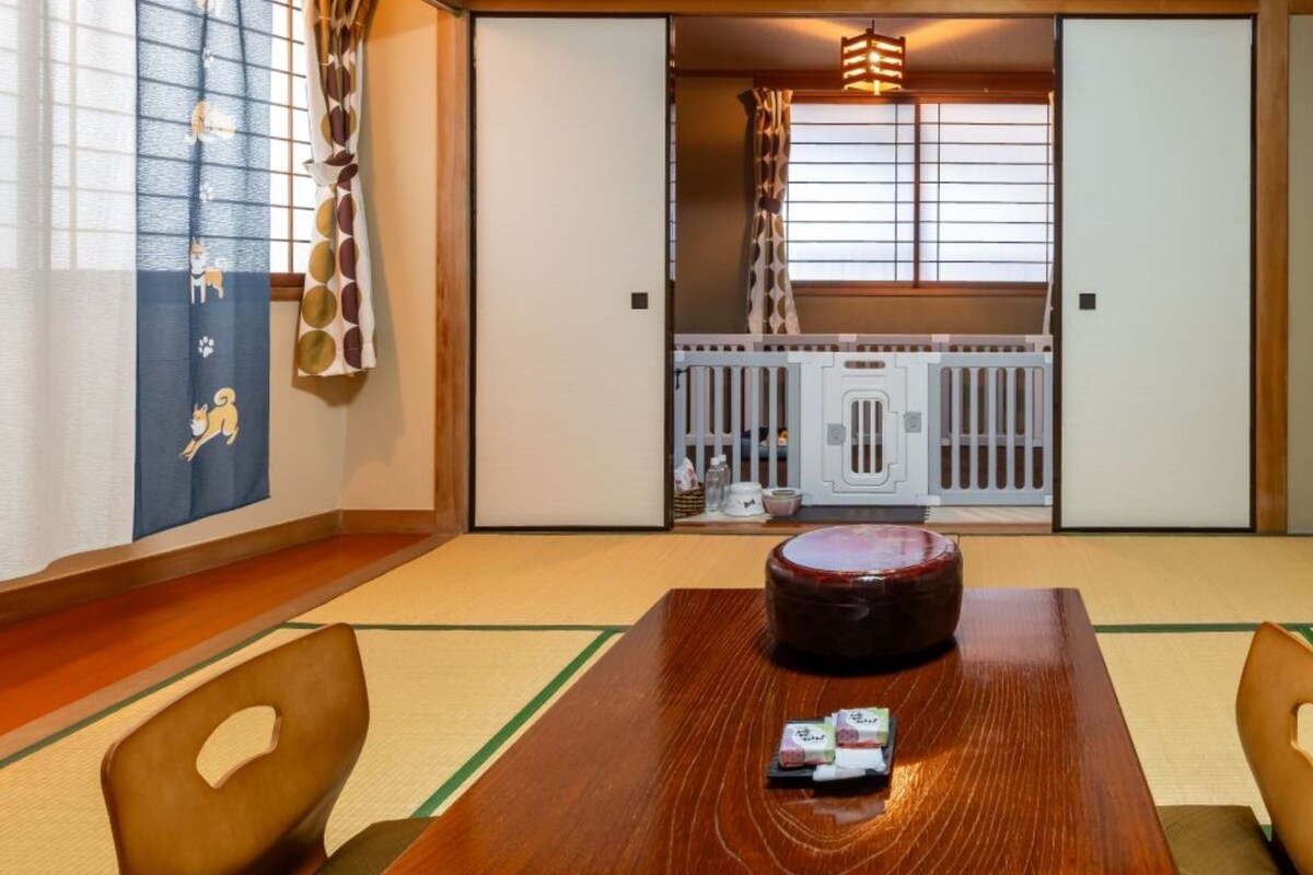 A traditional Japanese room with tatami flooring, a wooden table with a round tray, and a sliding door leading to a kitchen area.