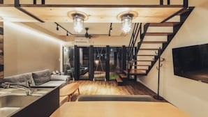 Ein modernes Interieur mit einer Couch, einem Esstisch, einer Treppe und einem an der Wand befestigten Fernseher.
