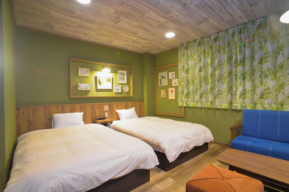 A room with two beds, a wooden ceiling, green walls, and a blue sofa.