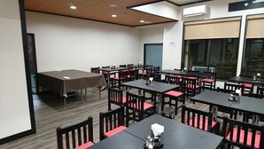 A conference room with multiple tables and chairs, a large table with a brown tablecloth, and a window with blinds. - Lupia Inn Nanko (Suwa)