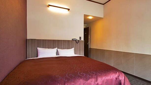 A hotel room with a large bed, a headboard, a wall-mounted light, and a door leading to another room. - Lupia Inn Nanko (Suwa)
