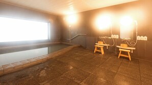 A sauna room with a large rectangular hot tub, wooden benches, and a wall-mounted sauna heater. - Lupia Inn Nanko (Suwa)