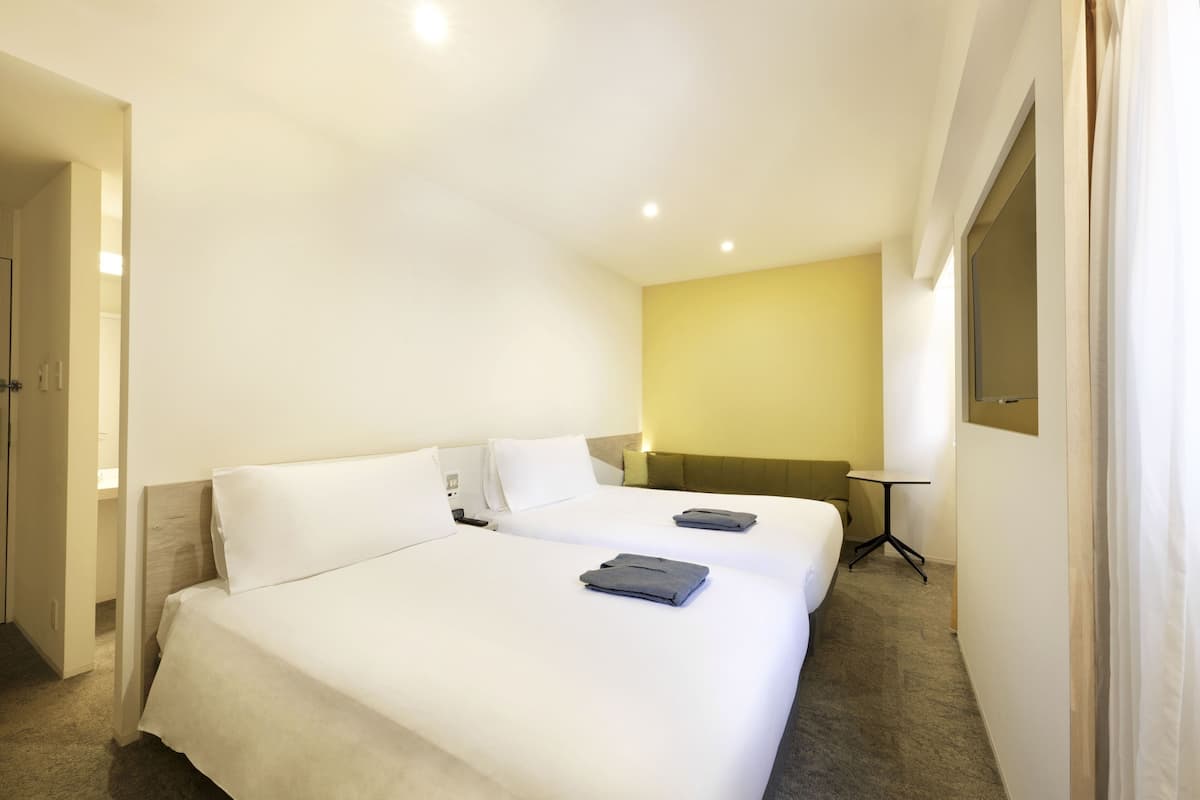 Une chambre d’hôtel avec deux lits, une petite table et une fenêtre.