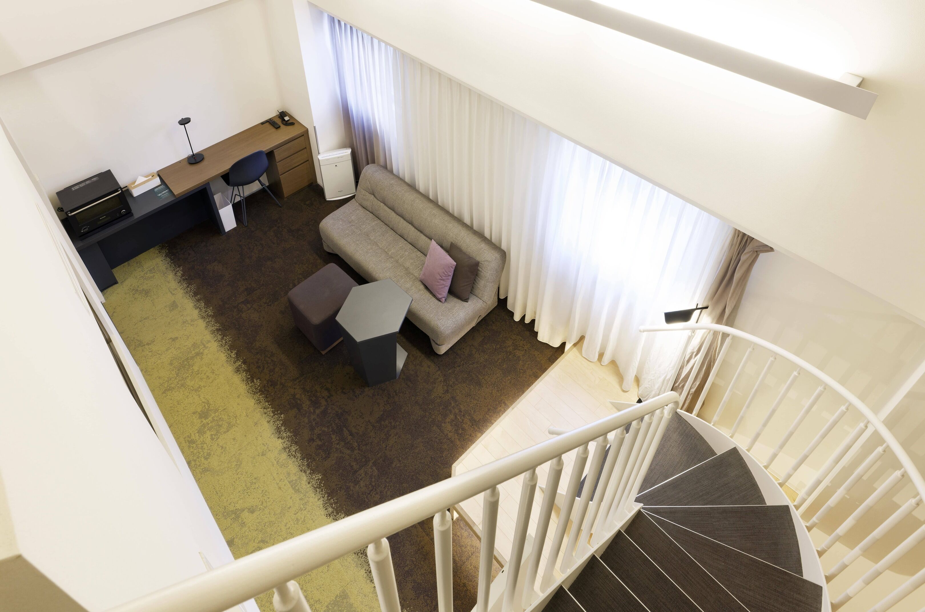 A modern interior with a sofa, a desk, and a staircase.