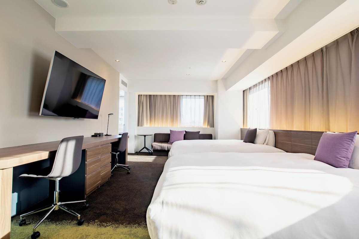 Une chambre d’hôtel avec un lit, un bureau, une chaise, une télévision et une fenêtre avec des rideaux.