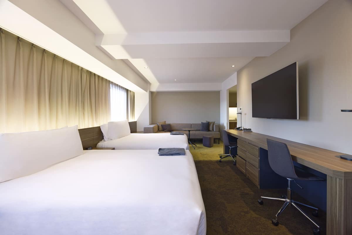 Une chambre d’hôtel avec deux lits, un bureau, une chaise, une télévision et un canapé.