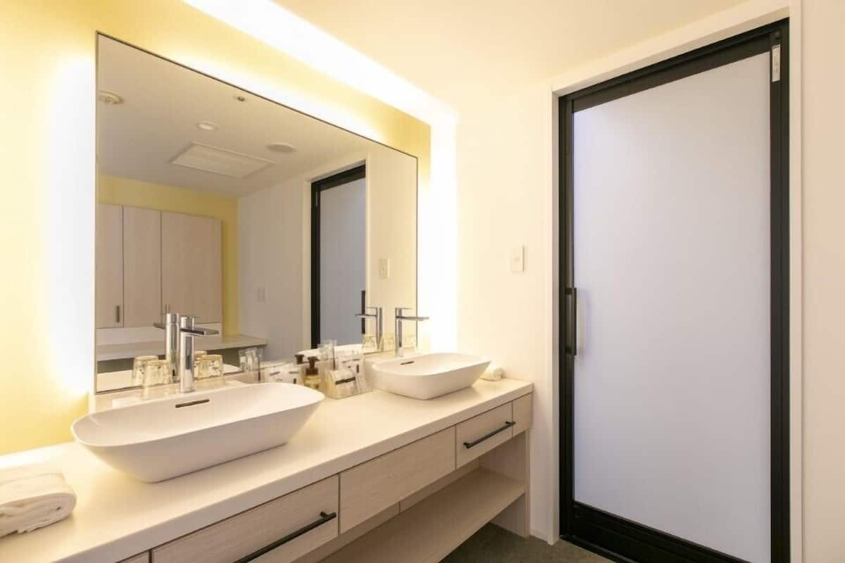 Une salle de bain moderne avec deux lavabos, un grand miroir et une porte.
