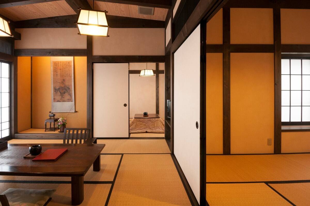Una habitación japonesa tradicional con suelo de tatami, una mesa baja con una carpeta roja y puertas correderas.