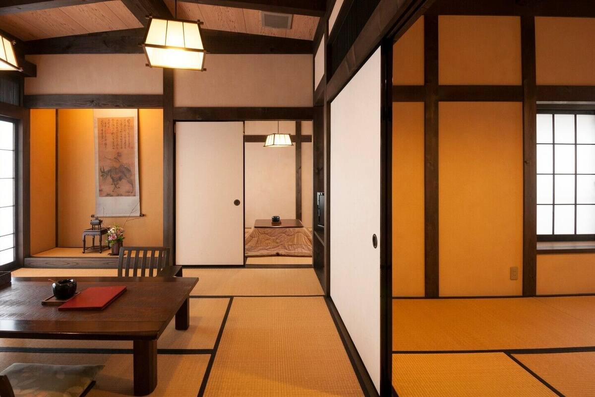 Una habitación japonesa tradicional con suelo de tatami, puertas correderas y una mesa baja con un tapete rojo.