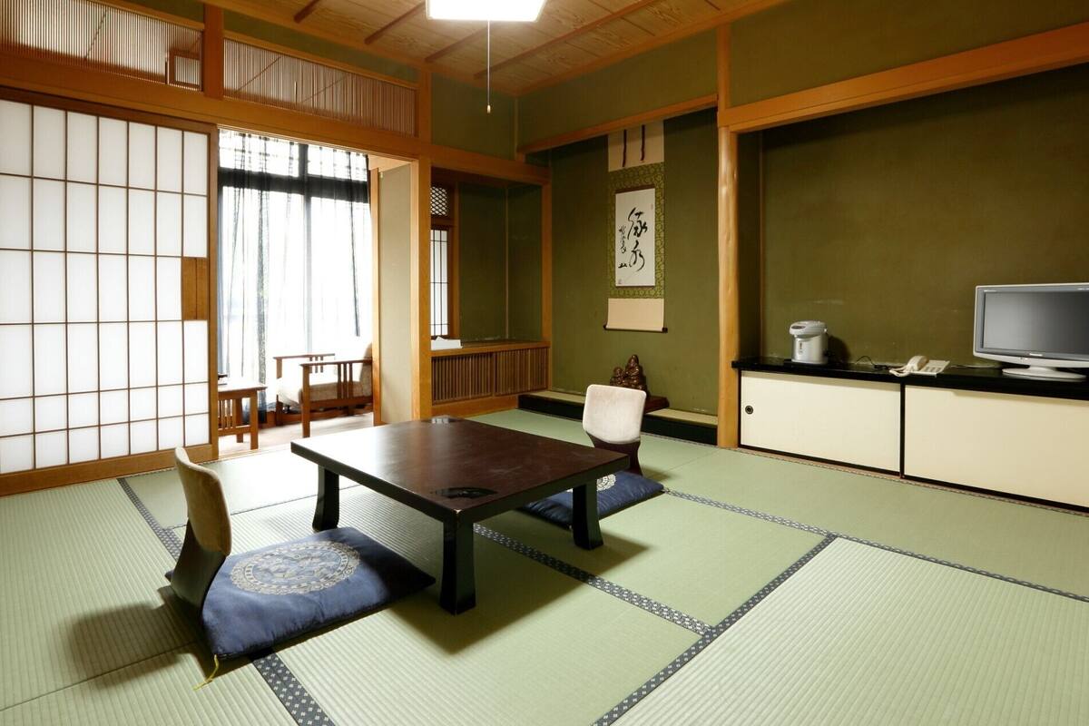 Una habitación tradicional japonesa con suelo de tatami, una mesa baja, una silla, un televisor y un armario.