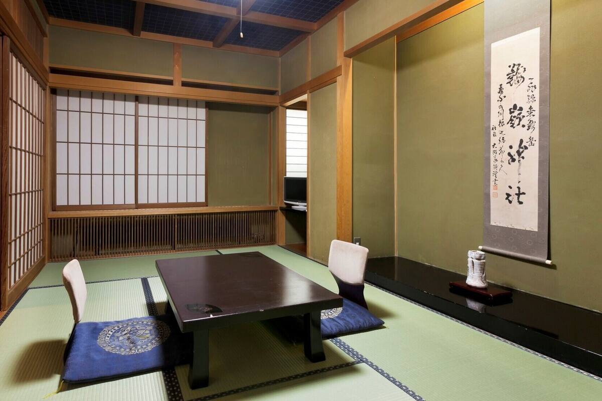 Una habitación japonesa tradicional con suelo de tatami, una mesa baja y un televisor sobre un mueble.