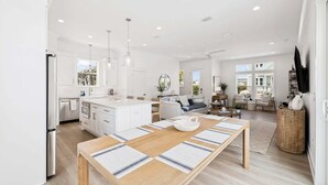 A spacious kitchen with a central island, a dining area with a long table, and a living area with a sofa and chairs. - Walk to Beach in Blue Mtn! Private Pool, LSV/Golf Cart, & Bikes! Sleeps 17! (Santa Rosa Beach)