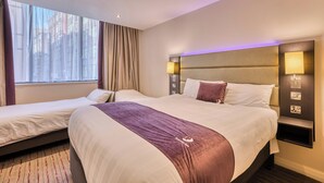 A hotel room with two beds, a large window with curtains, a headboard with integrated lighting, and a bedside table with a lamp. - Premier Inn Glasgow City Centre Hotel (Glasgow)